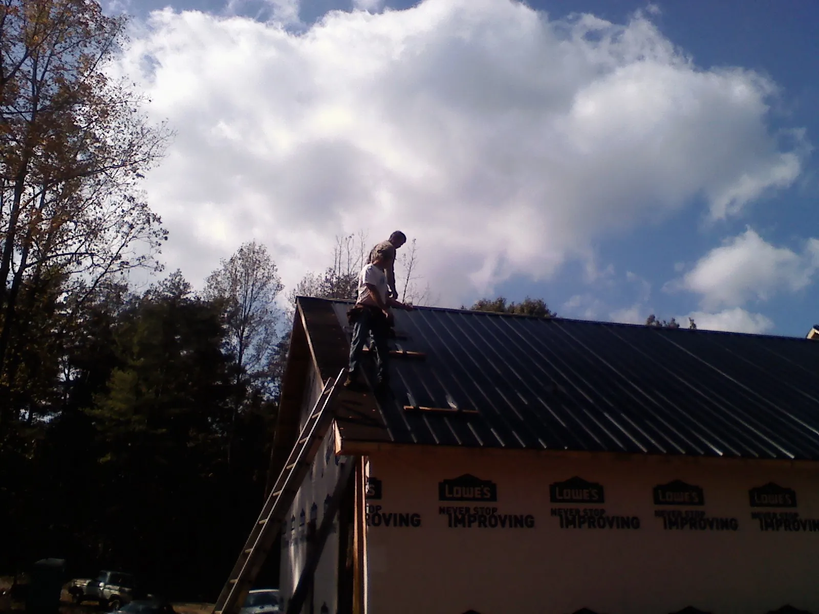 Roofer fastening dark metal panels high against a cloudy sky, from a Roof Inspection job in Paisley