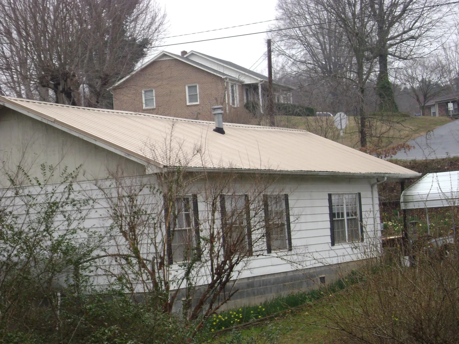 Tan metal roof on a white sided house set into a hillside — Commercial Roofing by Roofing Brothers in Paisley